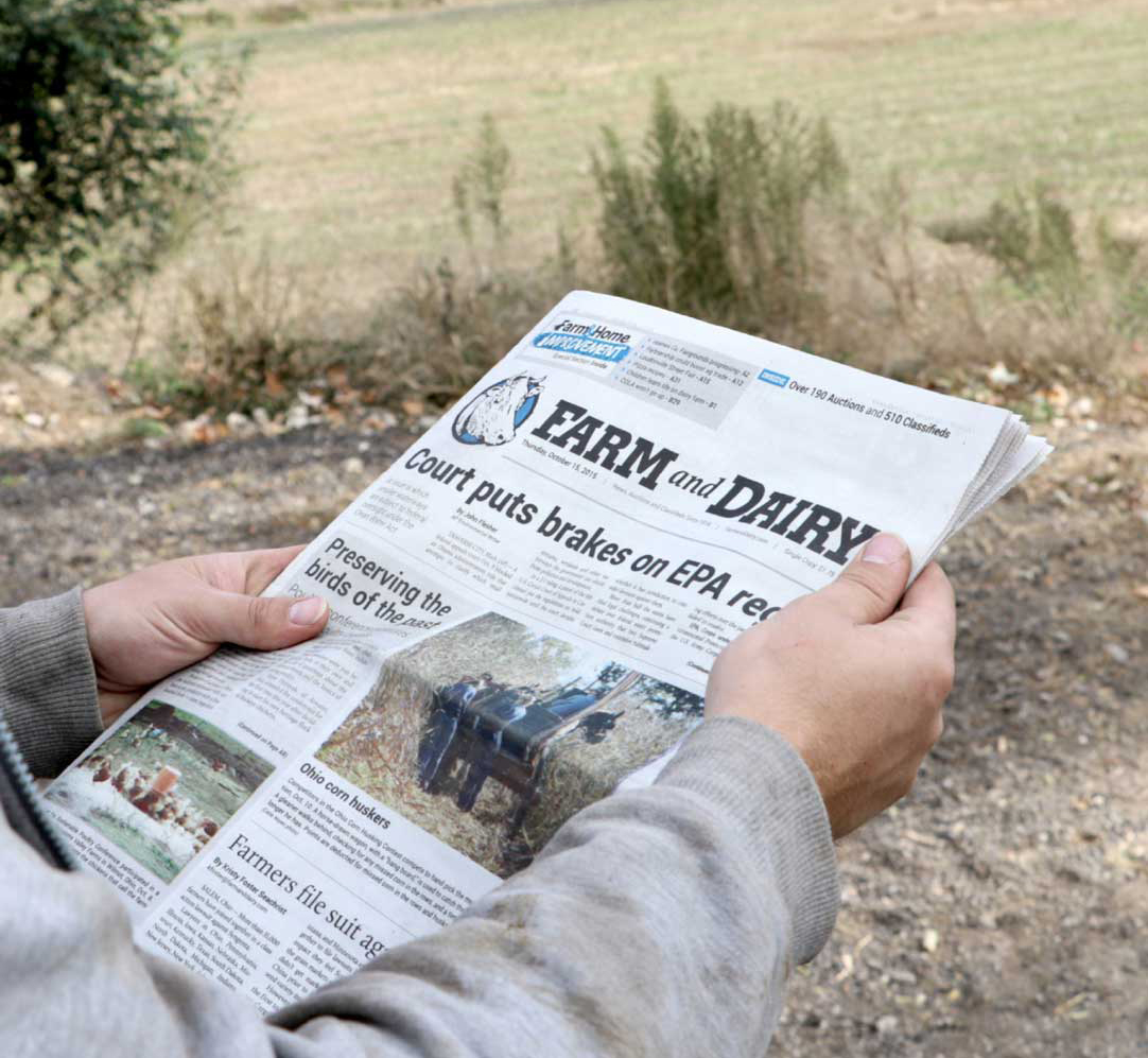 Man holding a Farm and Dairy Newspaper while out in the fields.