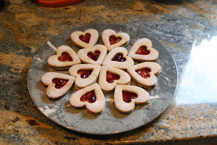A plate of heart shaped linzer cookies with raspberry filling.