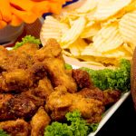 Ensure food safety while tailgating this football season Parmesan Wings with Super Bowl party snacks and a football in the background.