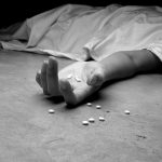 A black and white image of an addict, dead beneath a sheet, arm outstretched, pills in the palm of their lifeless hand and littering the floor near their hand.