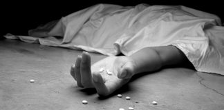About this series – Addiction: A Rural Reality A black and white image of an addict, dead beneath a sheet, arm outstretched, pills in the palm of their lifeless hand and littering the floor near their hand.