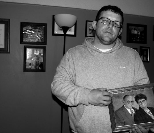 David Stanley’s last chance A man, David Stanley, stands holding his parents photo, behind him the wall is filled with other family photos. .