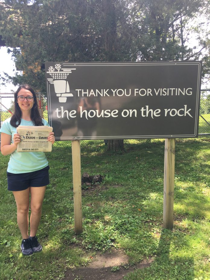 Lisa Kalas holding the Farm and Dairy Newspaper standing next to a sign that reads 
