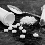 Pills, Fentynal Powder, and Heroin syringe sit on a table