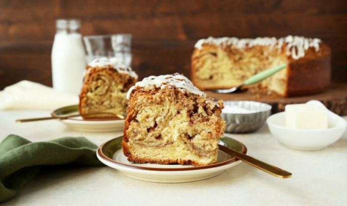 Cinnamon Roll Coffee Cake A slice of Cinnamon Roll Coffee Cake sits on a plate in the foreground with the remainder of the cake in the background.