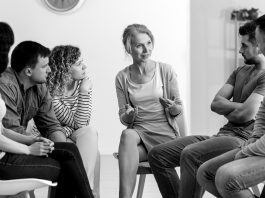 A diverse group of people sit and talk during a group counseling session.