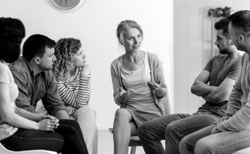 A diverse group of people sit and talk during a group counseling session.