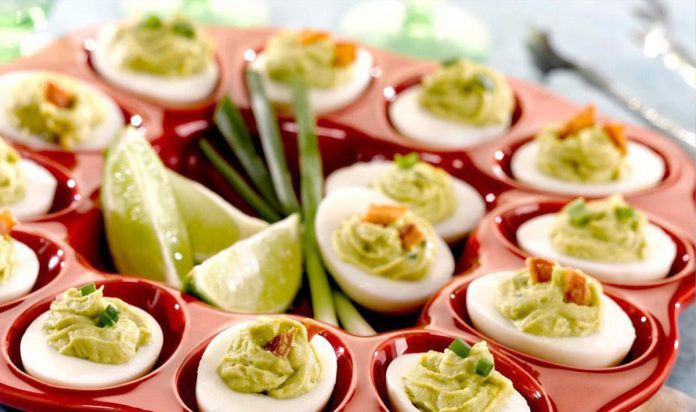 Guacamole Deviled Eggs A tray of Guacamole Deviled Eggs with cut limes in the middle of the tray.