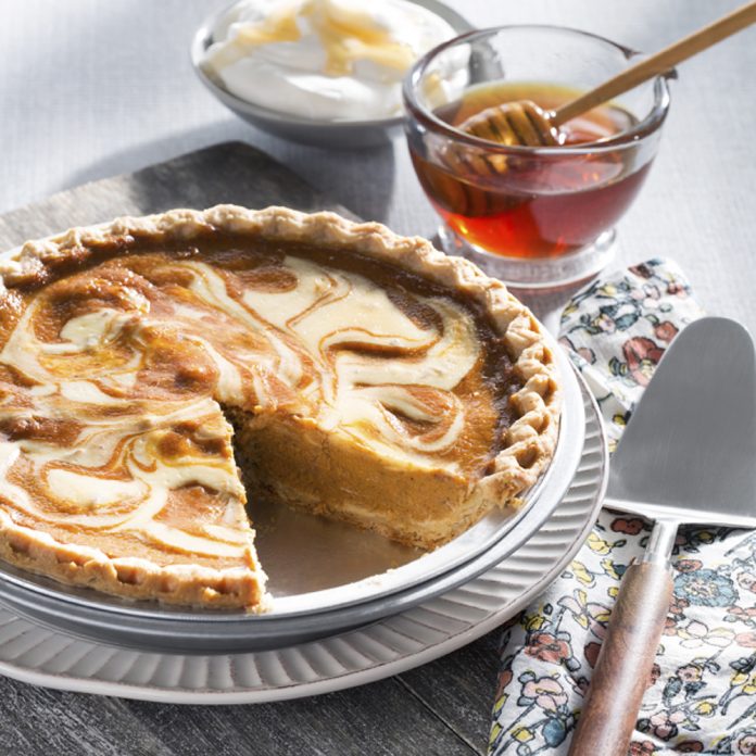 feature.web A Honey Cream Pumpkin Pie sits with one piece taken out of it. Two glass bowls, one filled with honey, the other filled with whipped cream, sit in the background of the image.