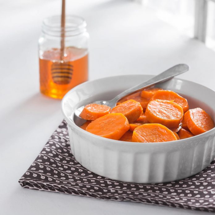 feature.web Candied Yams in a white serving dish with a glass honey container and dipper behind it.