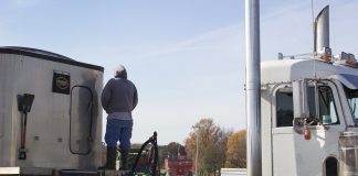 A farmer stands on a semi truck, watching combines harvest.