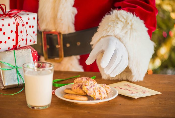 Santa reaching for cookies on a plate with a glass of milk nearby