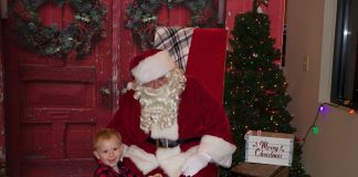 Santa visits dairy farm for milk and cookies A child sits on a yellow toy tractor in front of Santa.