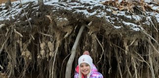 Vayda squatting in front of tree roots, holding soil together along a creek bed