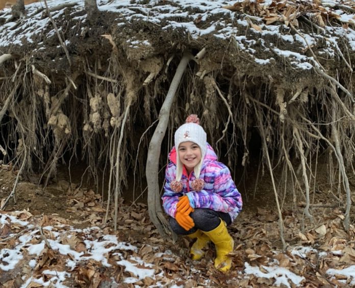 Vayda squatting in front of tree roots, holding soil together along a creek bed