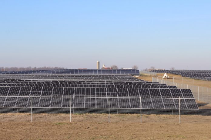 minster-ohio solar panels sit in a field with a barn and silo in the background