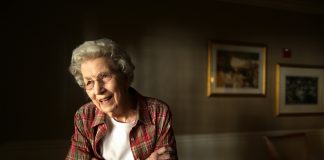A photo of Mildred Fizer, standing in a room in a red shirt.