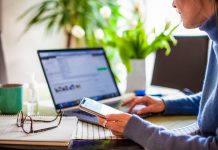 Why you need to check the FCC’s new broadband maps before Jan. 13 a person sits at a computer, holding a phone in one hand, with glasses on the desk next to her.