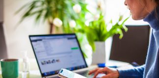 Why you need to check the FCC’s new broadband maps before Jan. 13 a person sits at a computer, holding a phone in one hand, with glasses on the desk next to her.