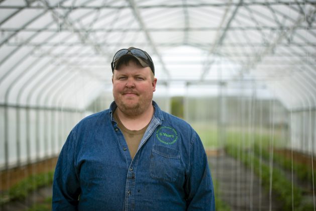 A man stands in a greenhouse on a farm.