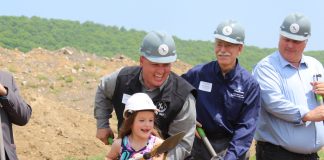 little girl shoveling dirt while wearing a hard hat