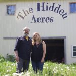 The Hidden Acres balances self-sufficiency with community A man and a woman stand in front of a barn with the words "The Hidden Acres" painted on it.