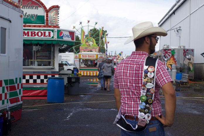 fair_travels_2 A 4-H'er shows off pins on his fair king sash on the midway at a fair.