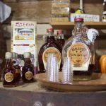 Bottles of maple syrup and small glasses set up for sampling on a table in a store.