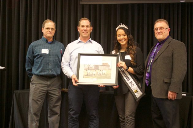Three men and a woman stand on stage with an award.