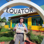 A Visit to the Ugandan Equator with Robin Tener Robin Tener stands inside the circular Ugandan Equator sign while holding a Farm and Dairy Newspaper.