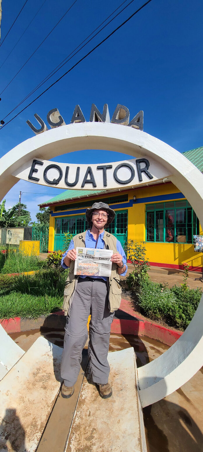 Robin Tener stands inside the circular Ugandan Equator sign while holding a Farm and Dairy Newspaper.
