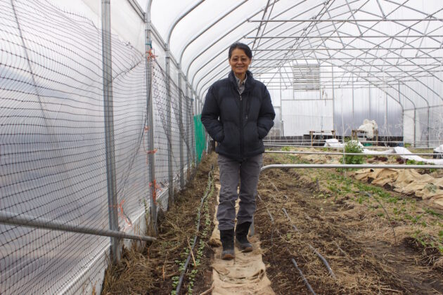A woman stands in a hoop house.