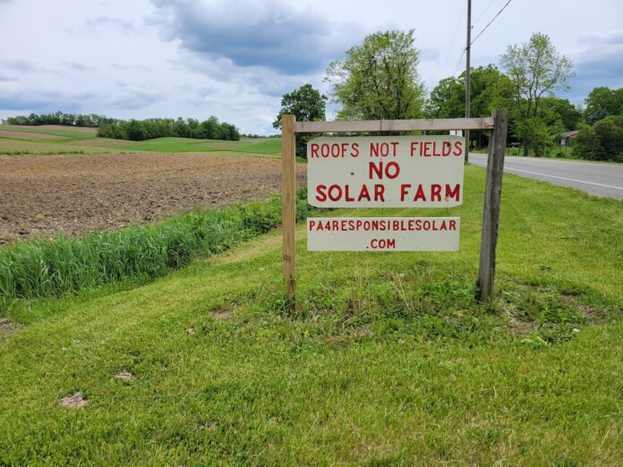 solar sign in lawrence county pa a sign reading roofs not fields no solar farm sits along a road with farm fields in the background