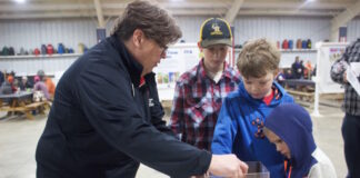A woman demonstrates the hazards of grain to three children with a mini gravity wagon.
