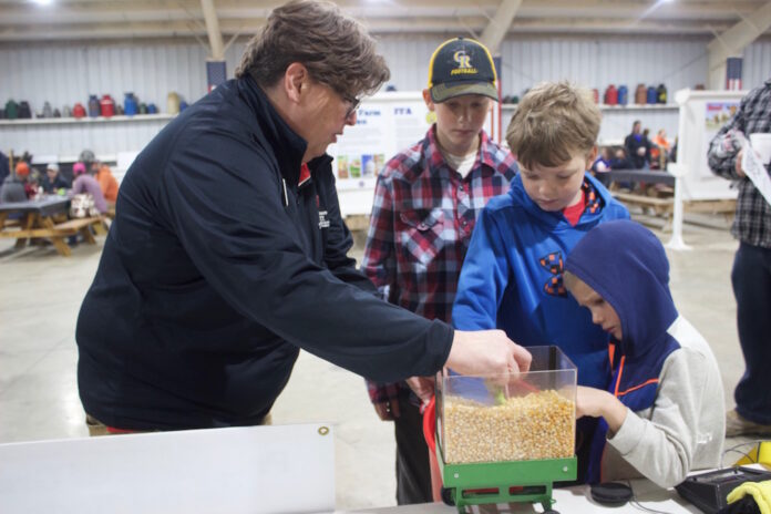 A woman demonstrates the hazards of grain to three children with a mini gravity wagon.