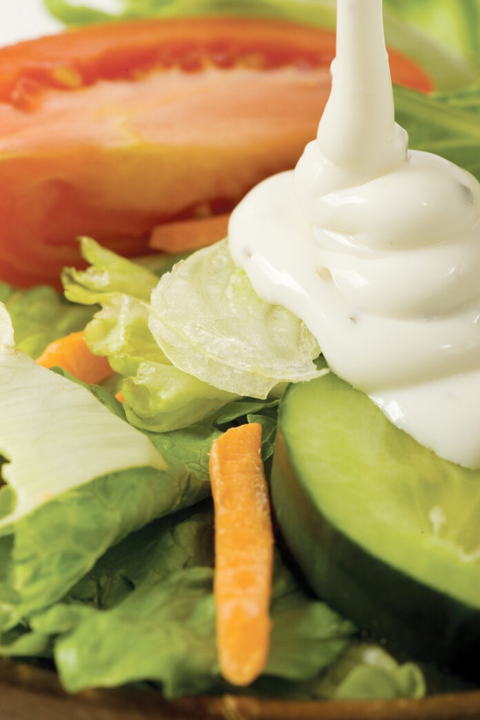 feature.web Ranch dresing pouring over a salad.