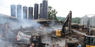 men watch an excavator dig in remains of a barn fire