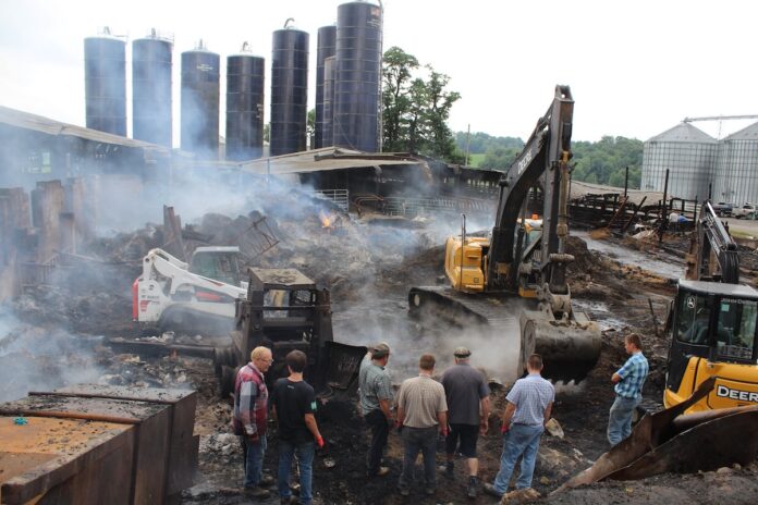 whiteleather-fire men watch an excavator dig in remains of a barn fire