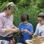 Children learn about agroforestry at Elder Tree Forest School a woman and two children cutting up ingredients for a salad.