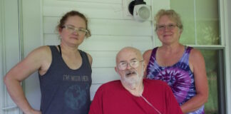 Two women and a man on the porch of a farmhouse.