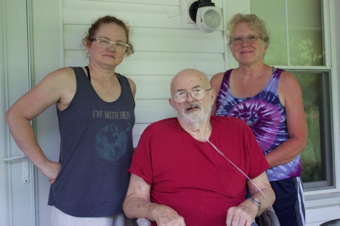 Two women and a man on the porch of a farmhouse.
