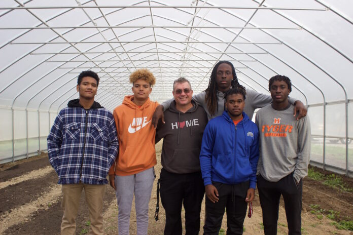 Five students and a teacher stand in a high tunnel