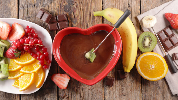 delicious chocolate fondue with fresh fruit in red heart bowl