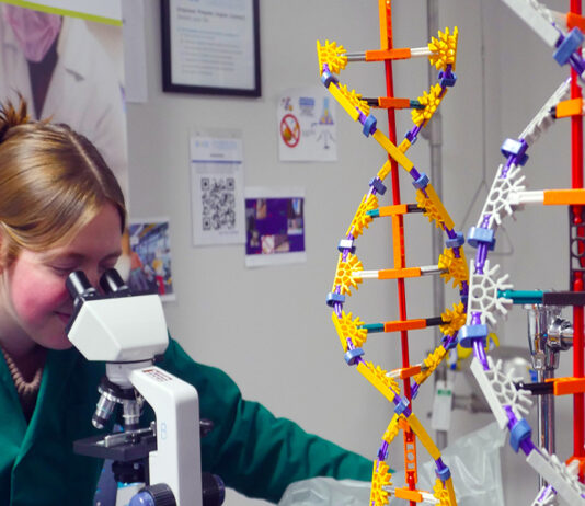 high school student looks through microscope with helix models on table