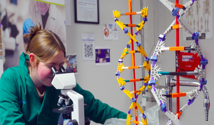 bioscience _header high school student looks through microscope with helix models on table