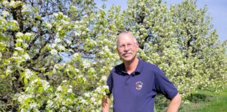 A white man stand in front of a tree with lots of white flowers on it