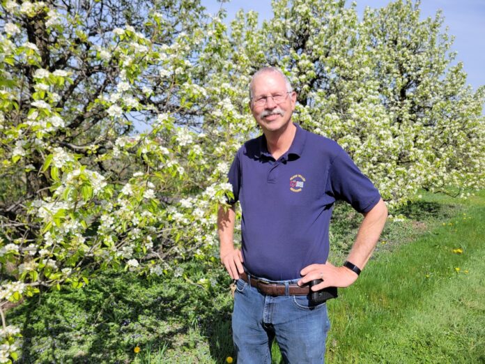A white man stand in front of a tree with lots of white flowers on it