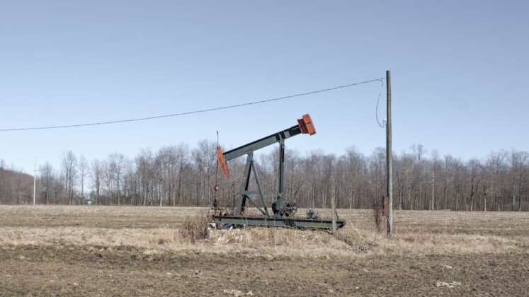 a pump jack sits in a the middle of a bare field
