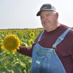 Ohio Agricultural Council announces 2024 Hall of Fame inductees dave brandt, a guru in no-till farming practices, stands wearing blue jean bib overalls in a field of sunflowers