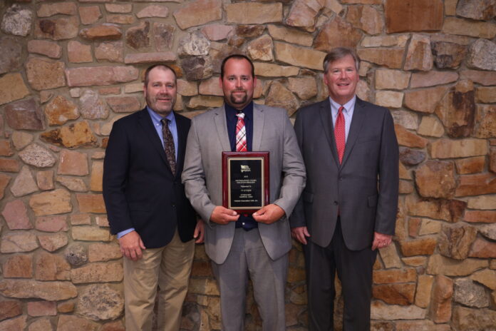 three men stand together while the one standing in the middle holds a plaque